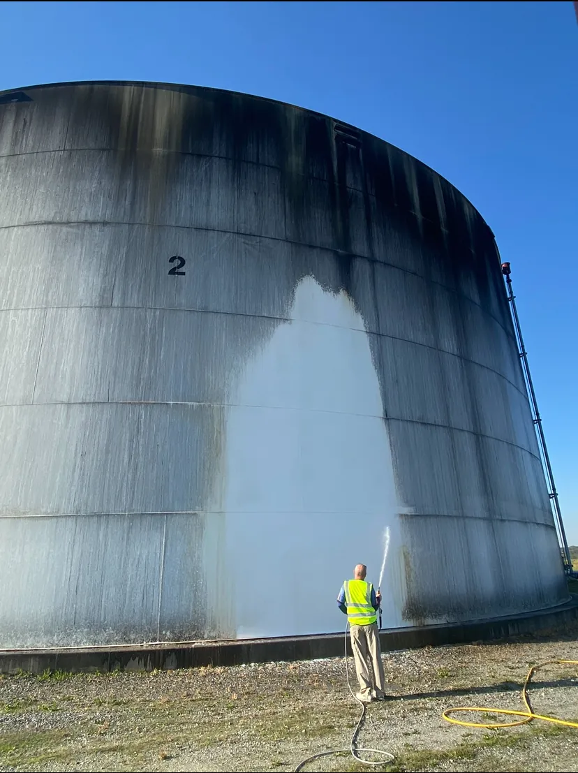 A crew member washing a clean stripe up a large storage tank